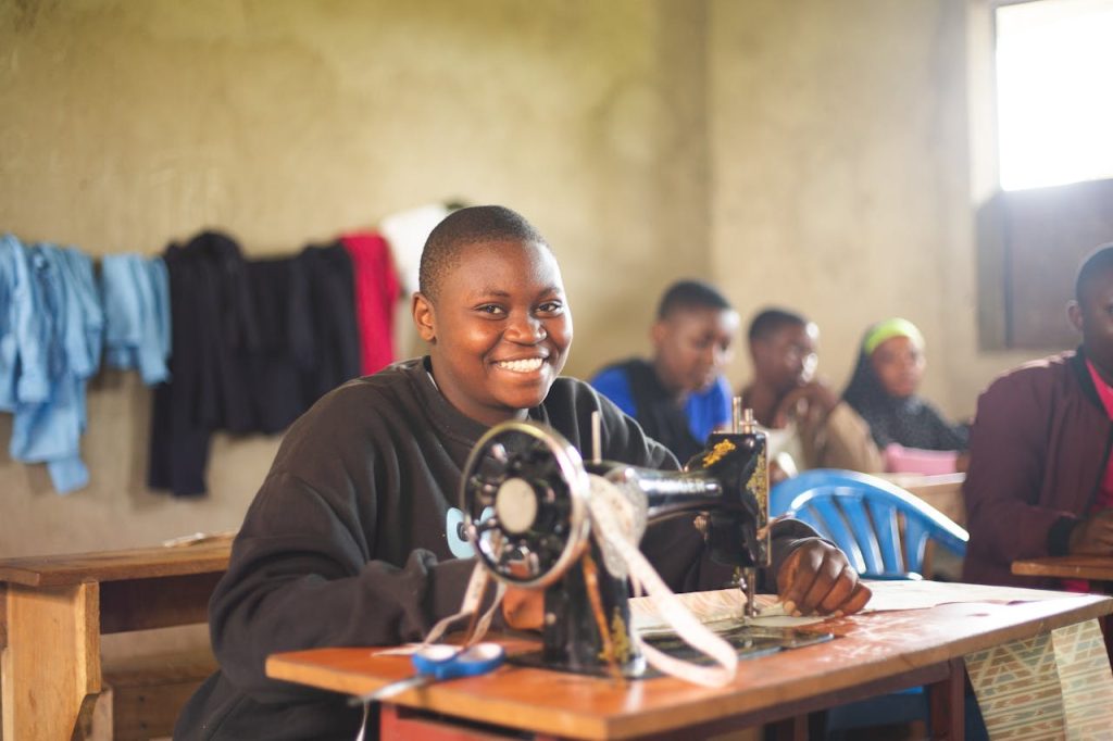 students-in-a-class-with-a-sewing-machine-20853652 Happy student in Uganda using sewing machine in class, highlighting education.